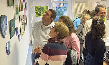 3 Besucher*innen der Ausstellungseröffnung "Lust auf Farbe" betrachten gemeinsam ein Bild